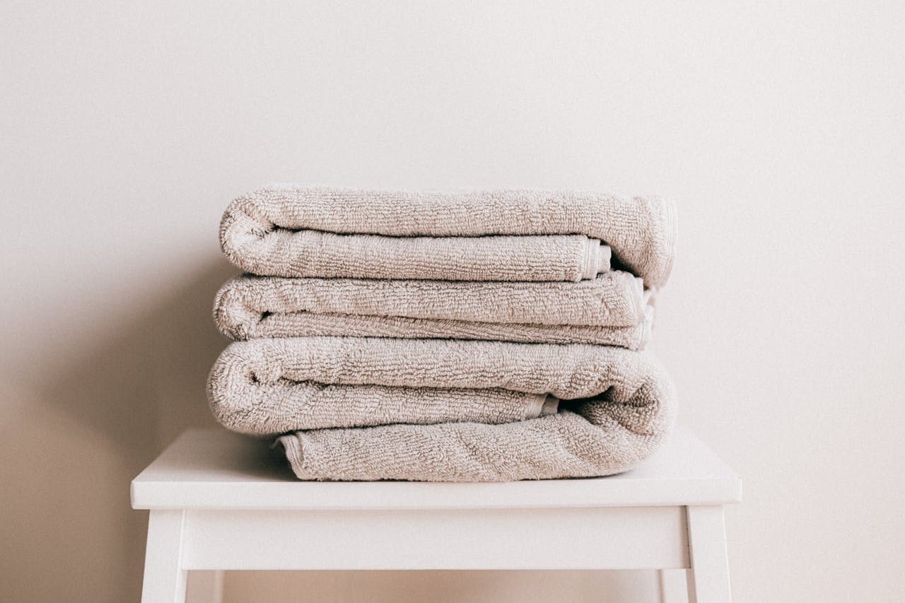 Home Stack of soft clean light beige folded towels placed on white minimalist stool against beige wall in daylight