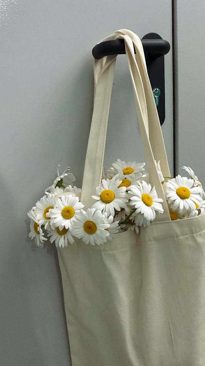 About A stylish tote bag overflowing with vibrant daisies against a simple backdrop.