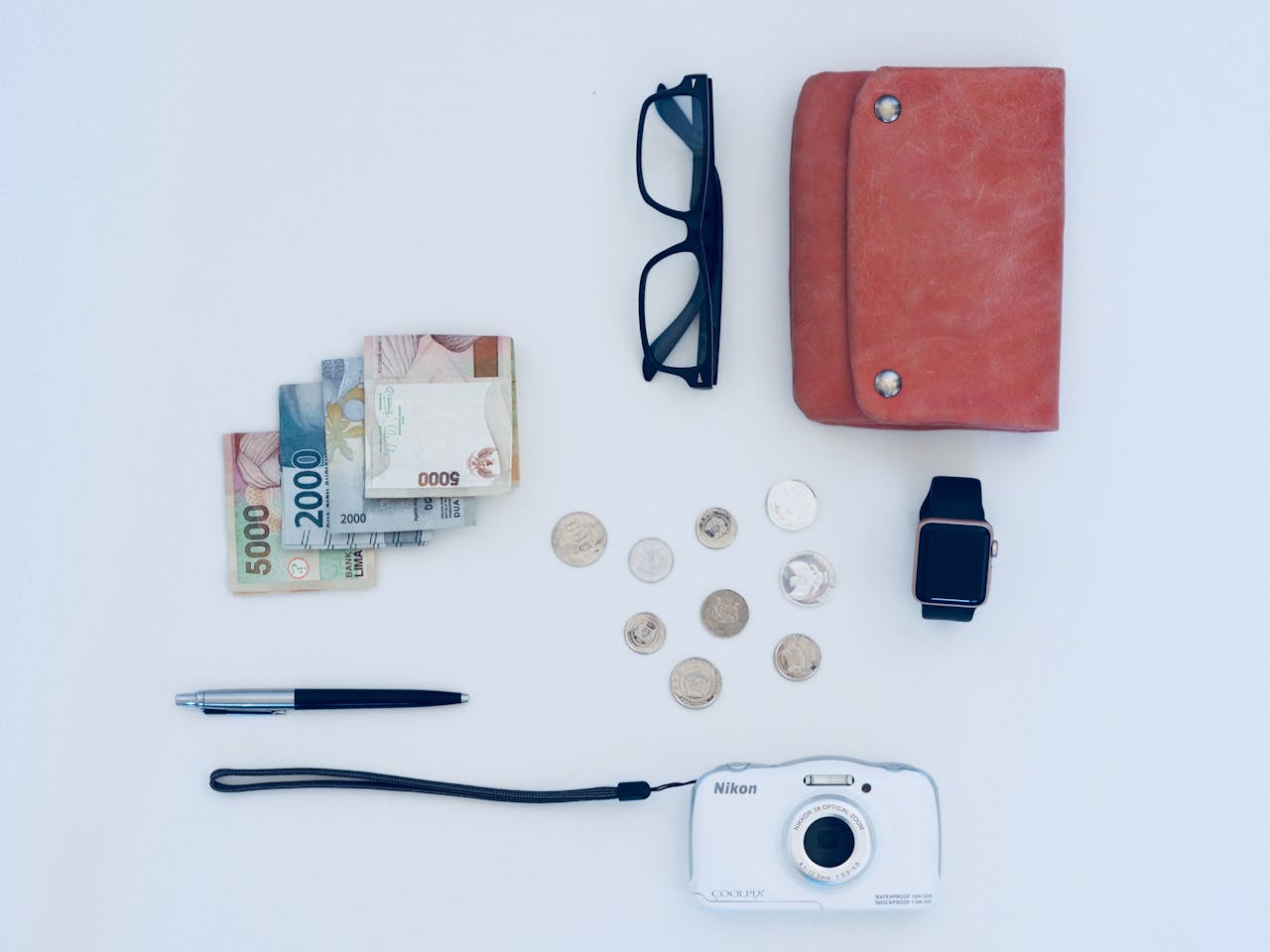 Home Flat lay of everyday items including currency, coins, wallet, and gadgets, all on a white background.